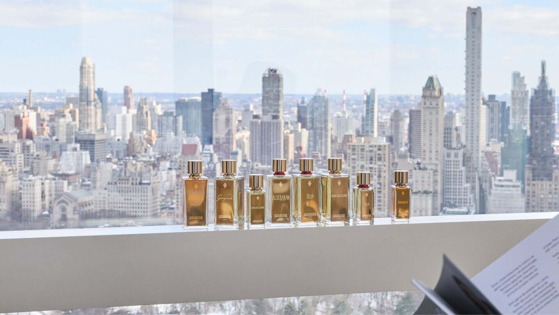 Collection of luxurious fragrances displayed on a windowsill with a city skyline backdrop.